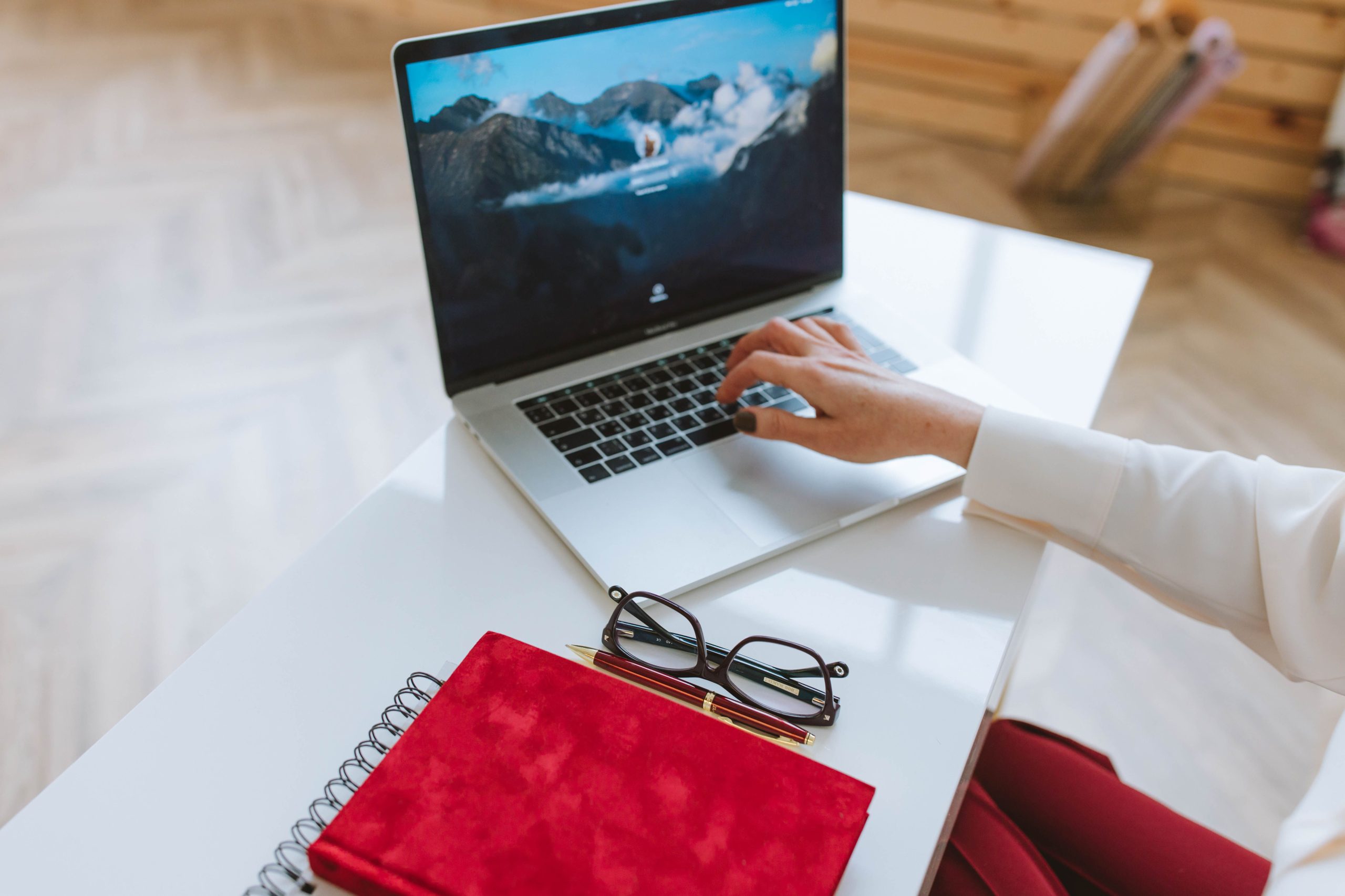 Personne travaillant sur laptop avec carnet rouge et lunettes