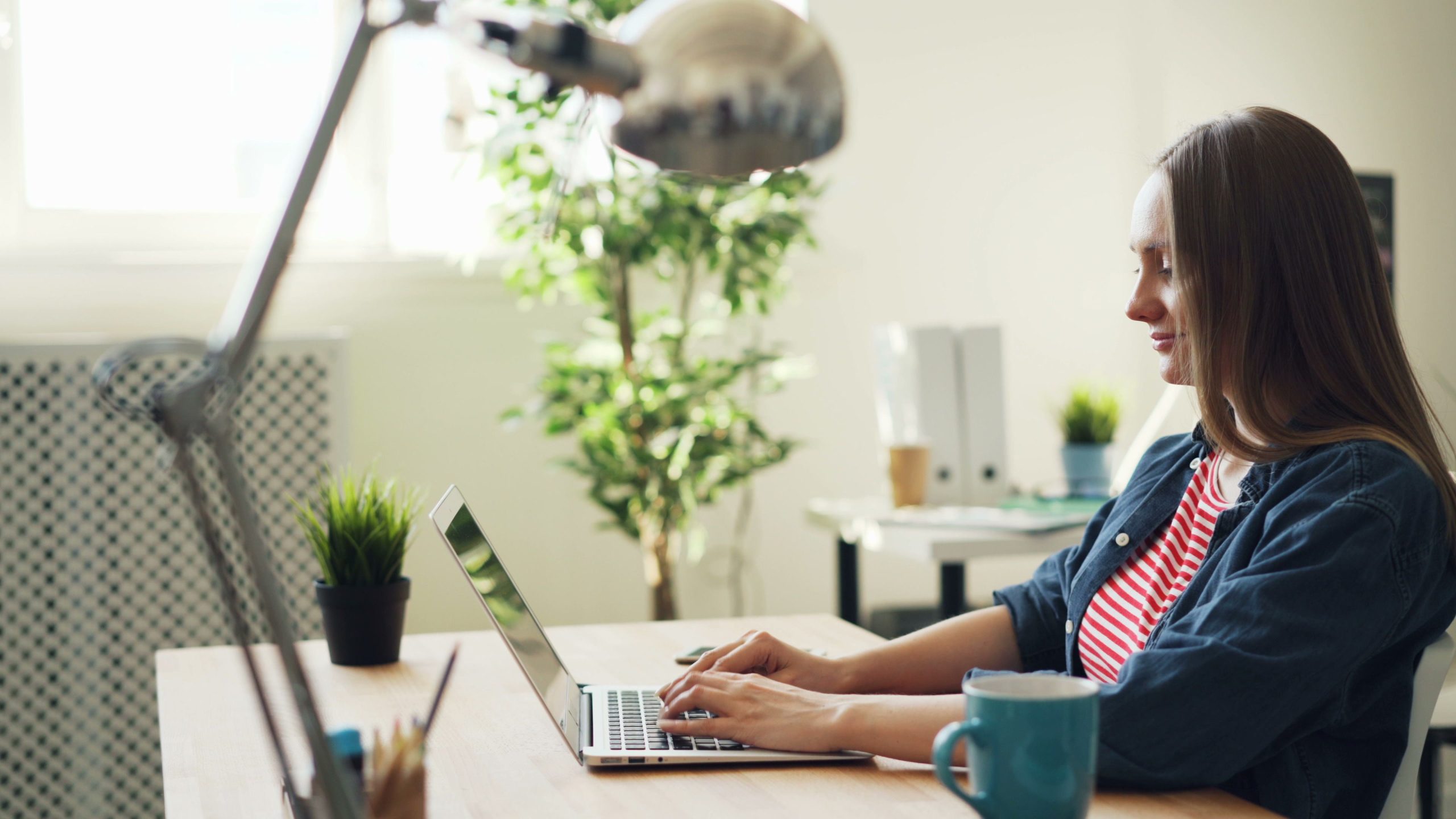 Femme souriante travaillant sur laptop au bureau avec plantes