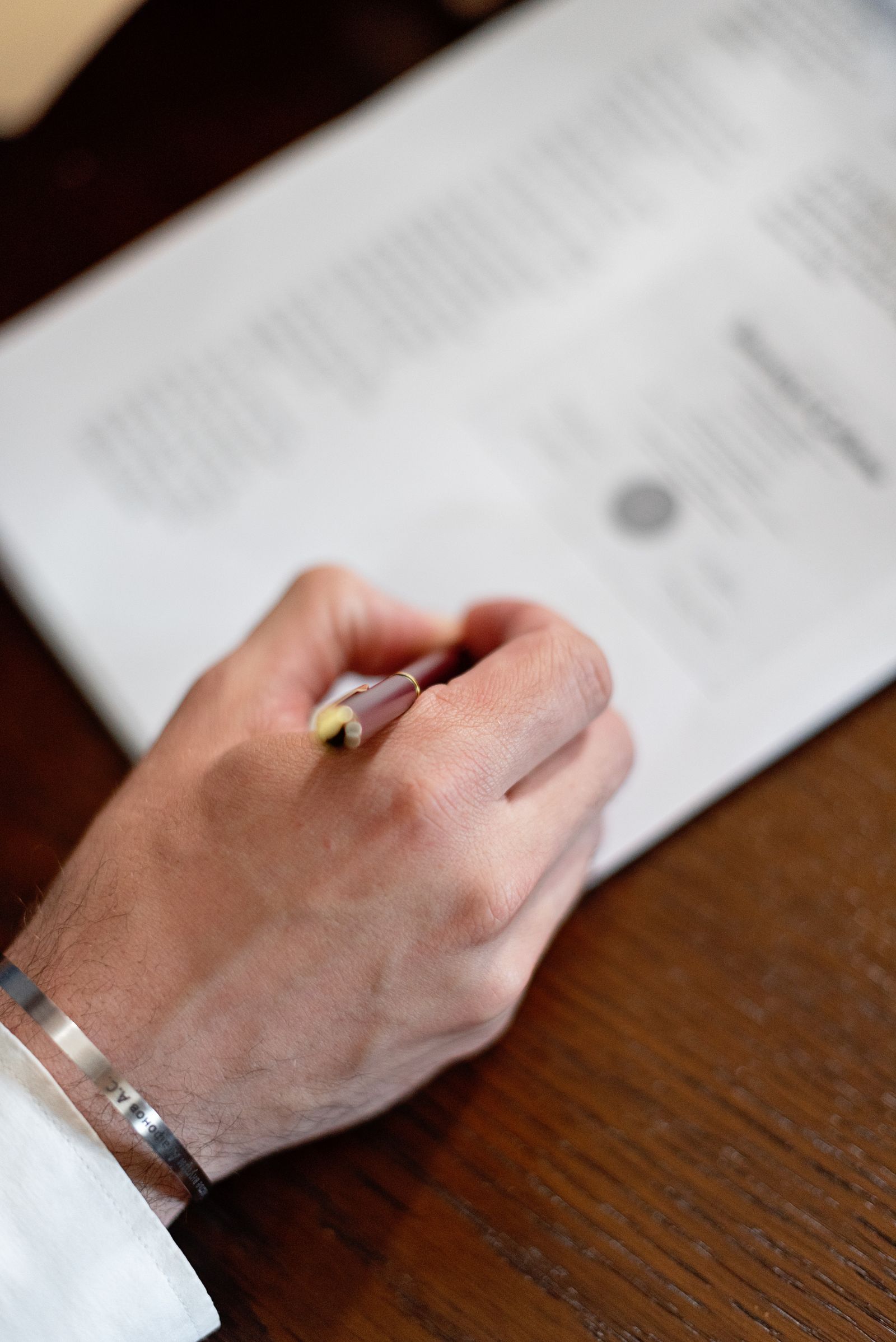 Main qui signe un document au stylo sur une table en bois